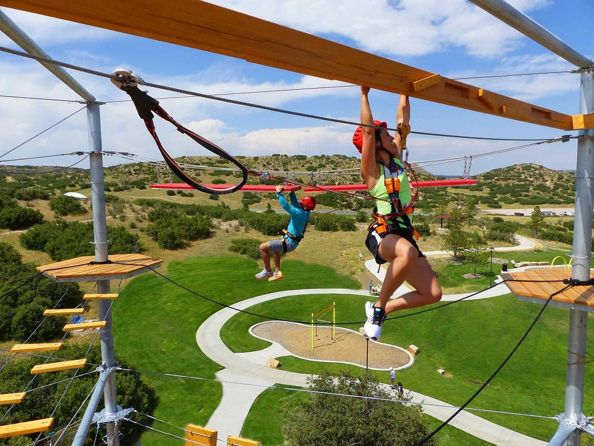 Guests on The Edge Zipline sky-trek aerial adventure course with harnesses, helmets, and Colorado high-desert landscape below